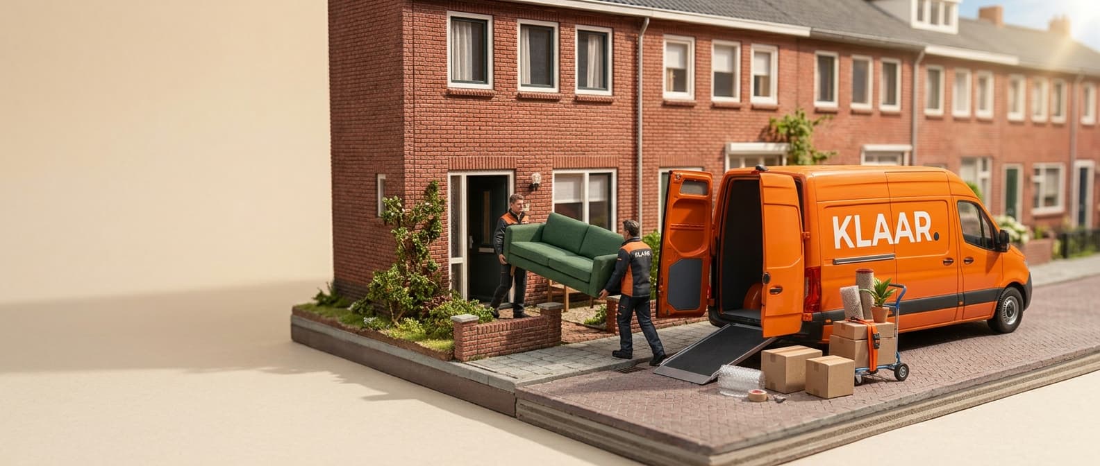 Miniatuurmodel van een Nederlandse rijtjeshuisstraat: twee verhuizers dragen een groene bank uit de voordeur naar een oranje KLAAR-bestelbus met open achterdeuren, met een oprijplaat, een steekwagen en verhuisdozen op de stoep.